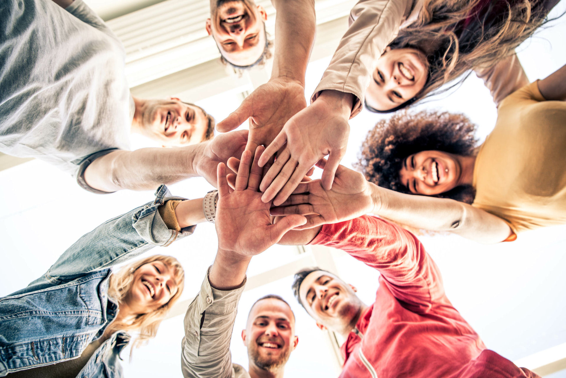 Mixed-gender sobriety support group looking down as they bring their hands together for a circular cheer